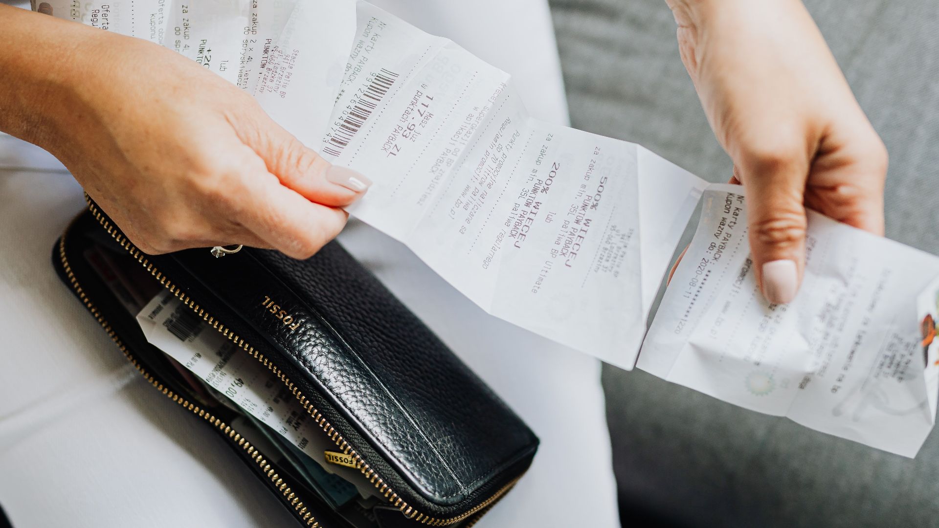 Close-up of a woman's hands managing multiple receipts taken from a black wallet.