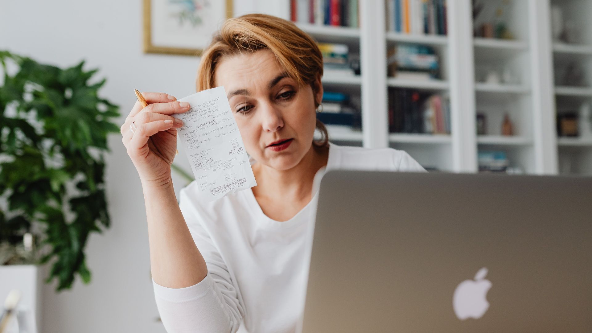 Woman concentrating on receipts while using a laptop, reflecting financial stress.