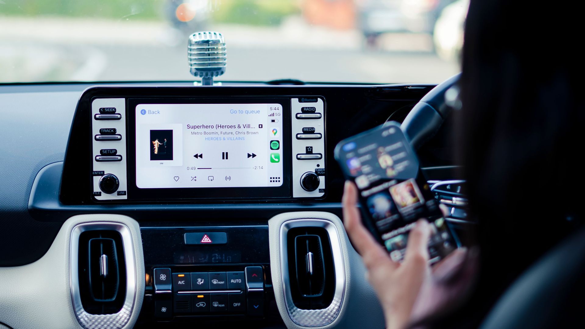 Car dashboard with a touchscreen display and person using a smartphone inside a vehicle.