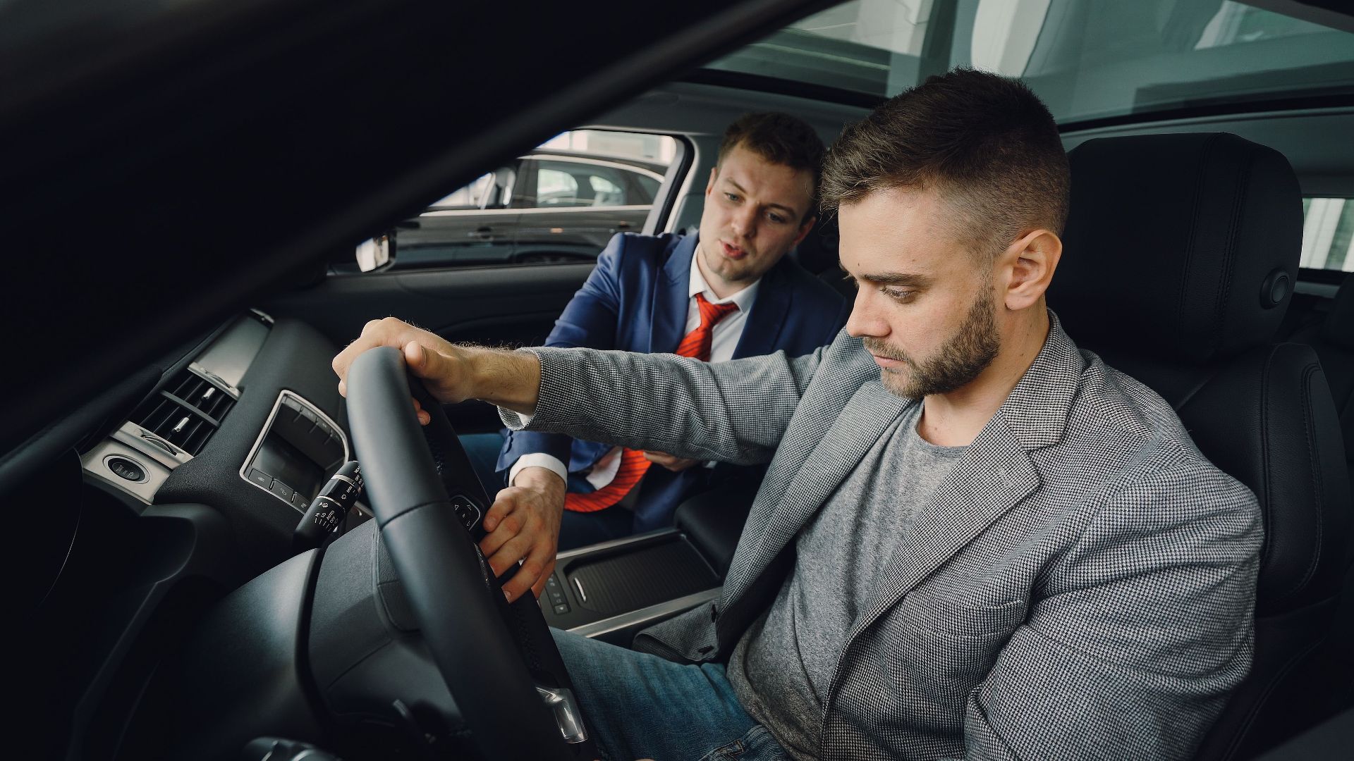 Salesman demonstrating car features to potential buyer inside vehicle showroom.