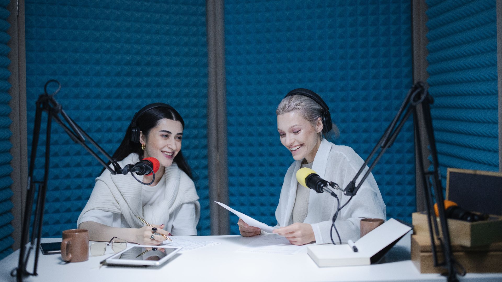 Two women recording a podcast in a soundproof studio with professional equipment.