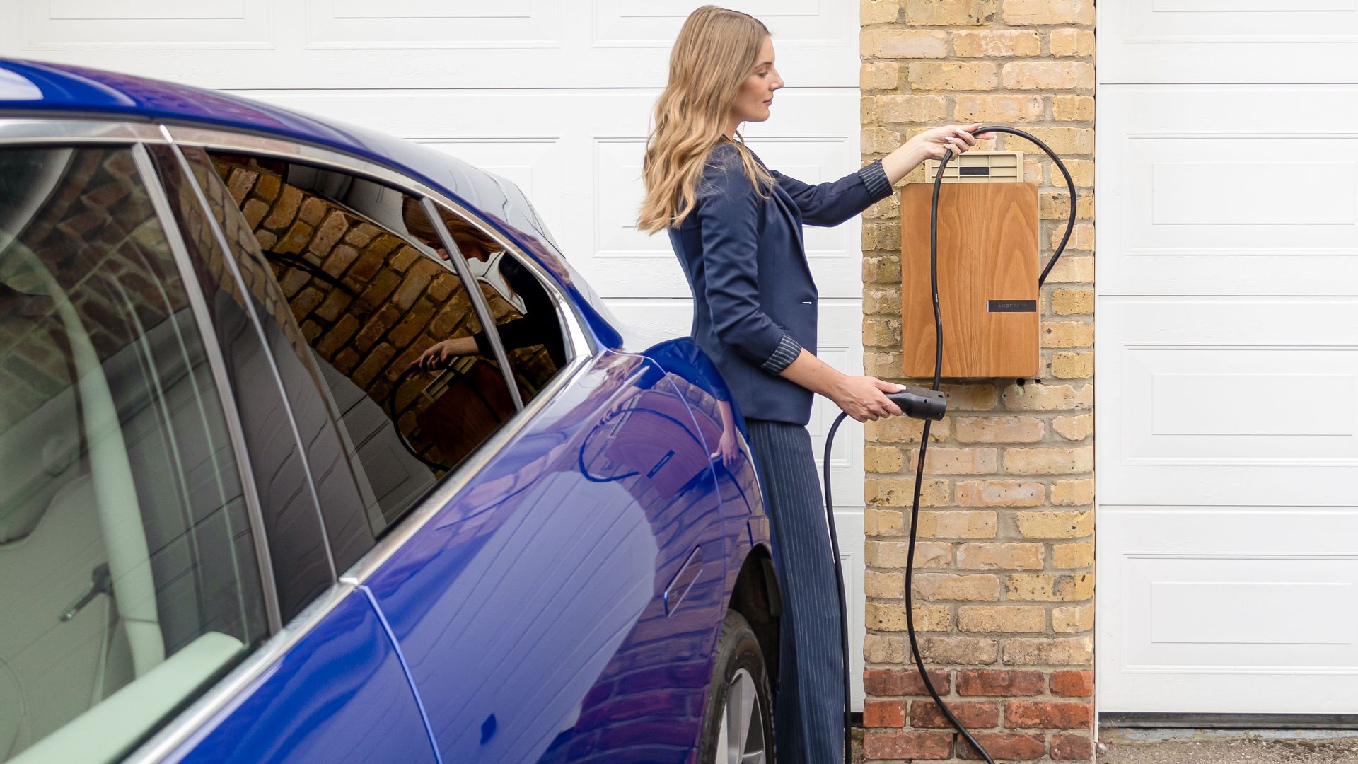 A woman efficiently charges her blue electric car at a home EV charging station.