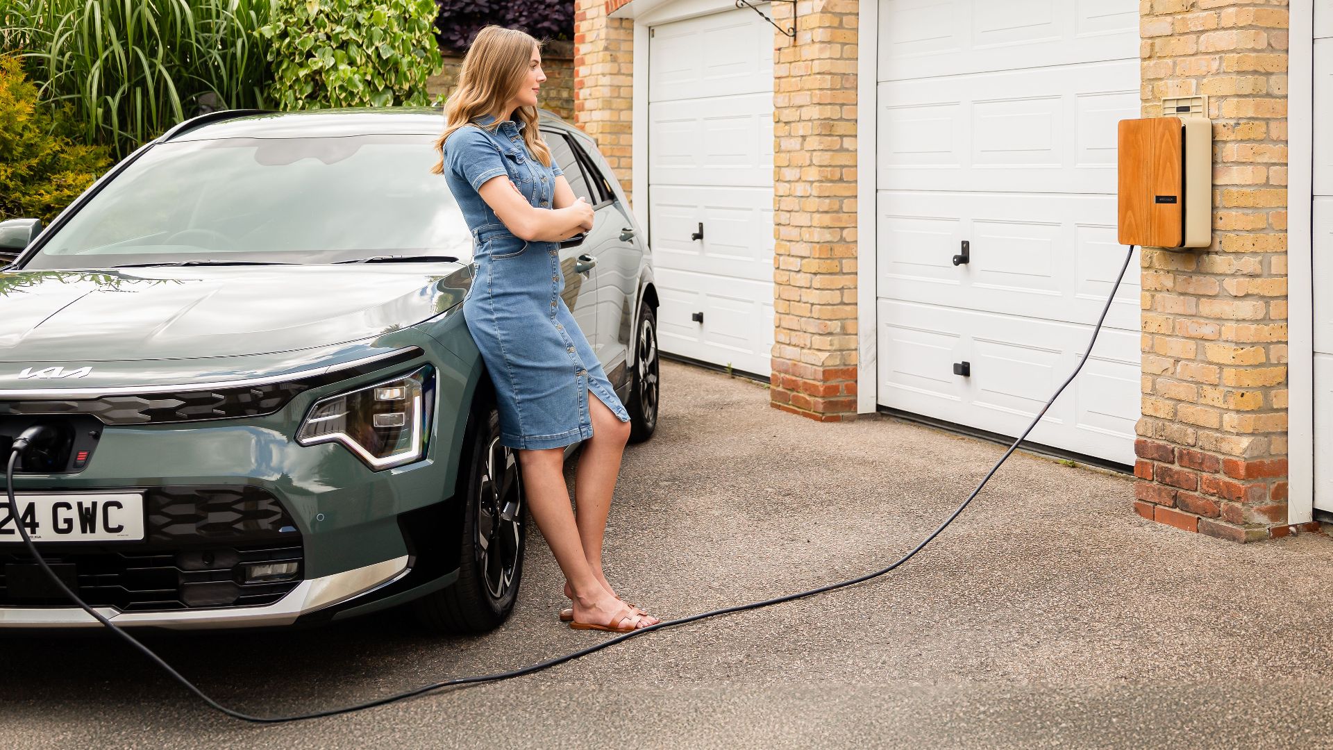 Woman charging electric vehicle at home with a modern wall-mounted charging station.