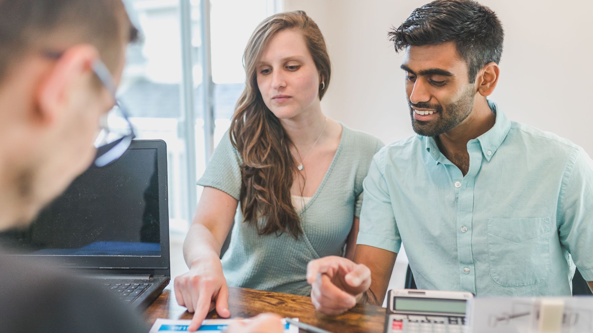 Young couple consulting with a financial advisor using a calculator and documents in a bright office setting.