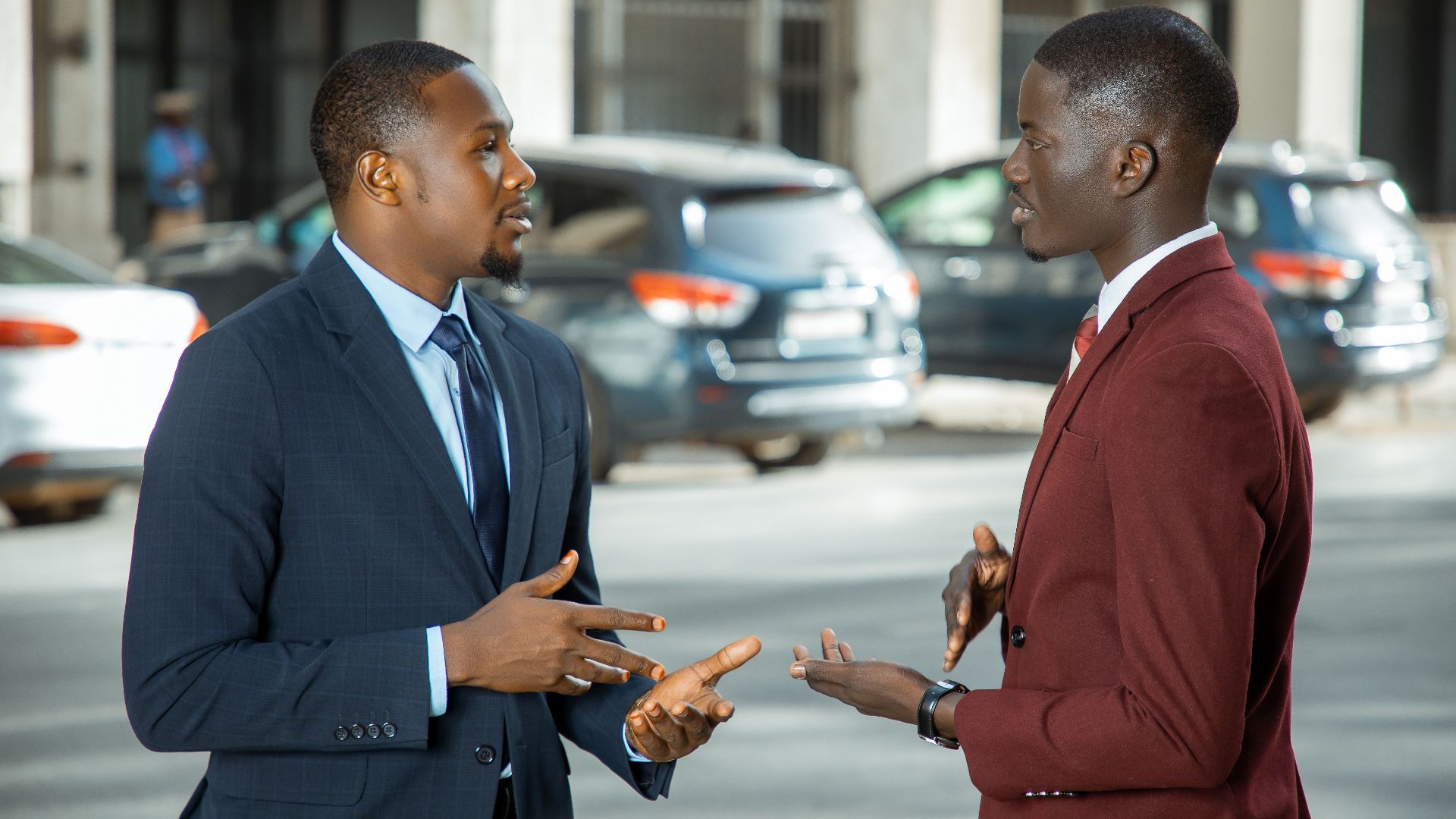 Two African businessmen in formal suits have a discussion on a city street in Dakar, Senegal.