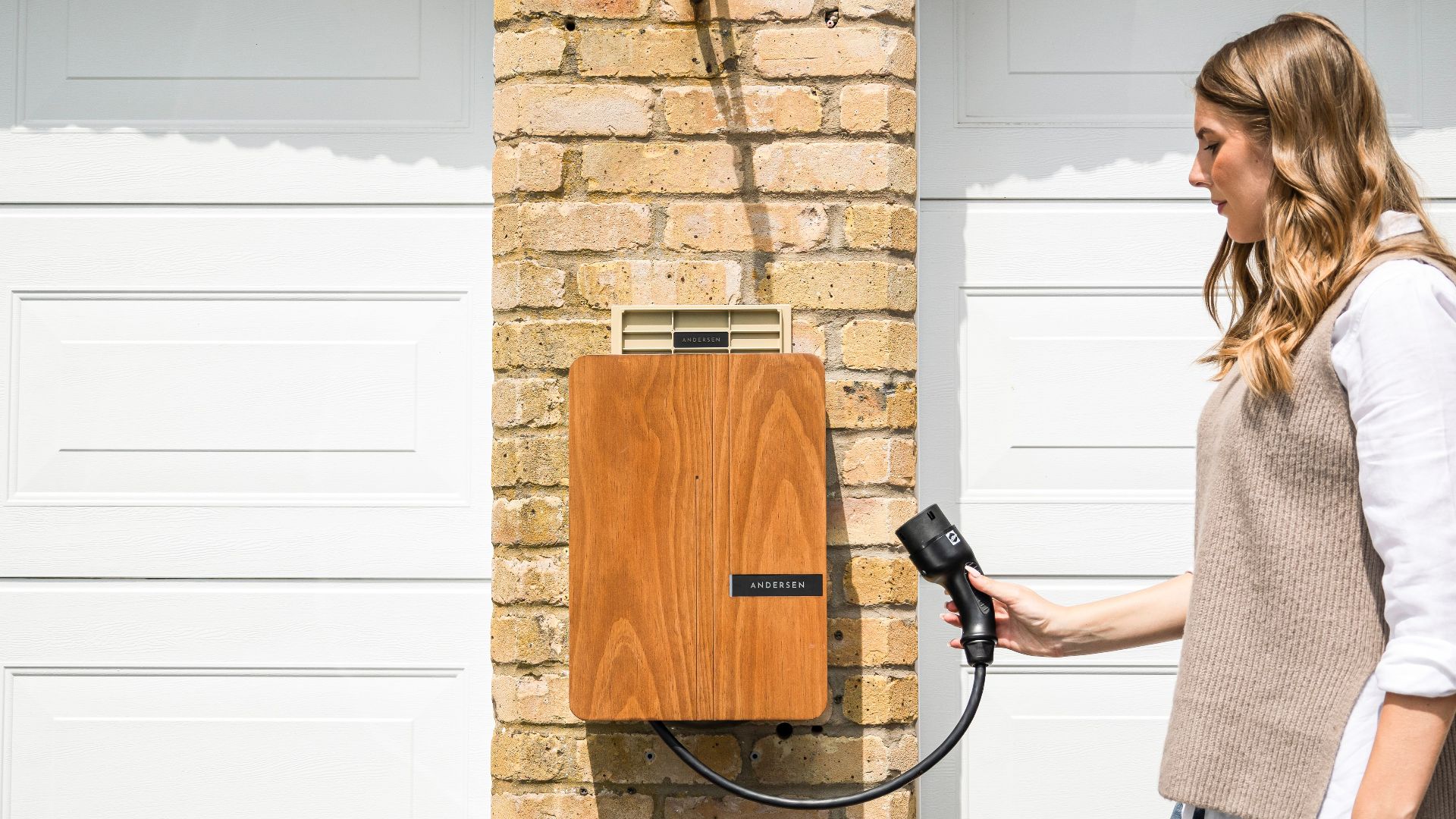 A woman uses a home electric vehicle charger mounted on a brick wall.