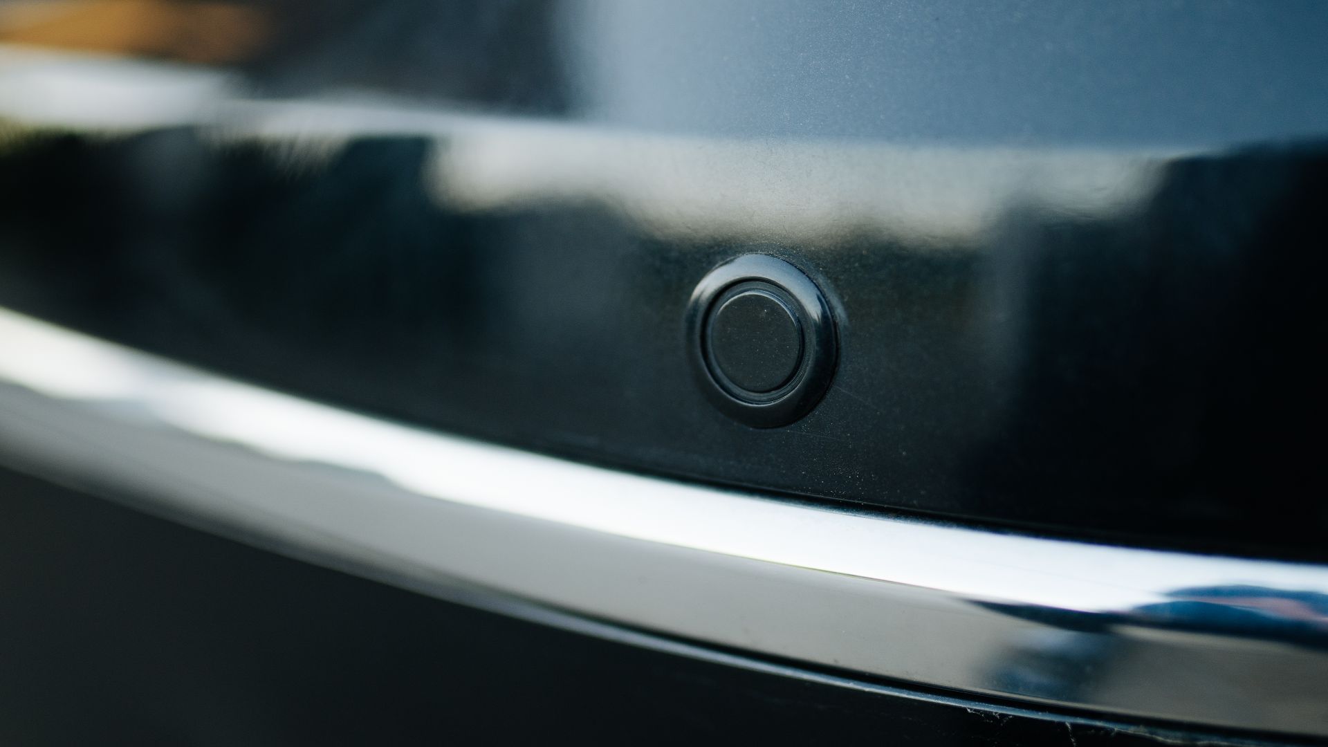 A shiny black surface features a small circular button, showcasing modern design elements and craftsmanship. The focus emphasizes smooth textures and details in lighting.