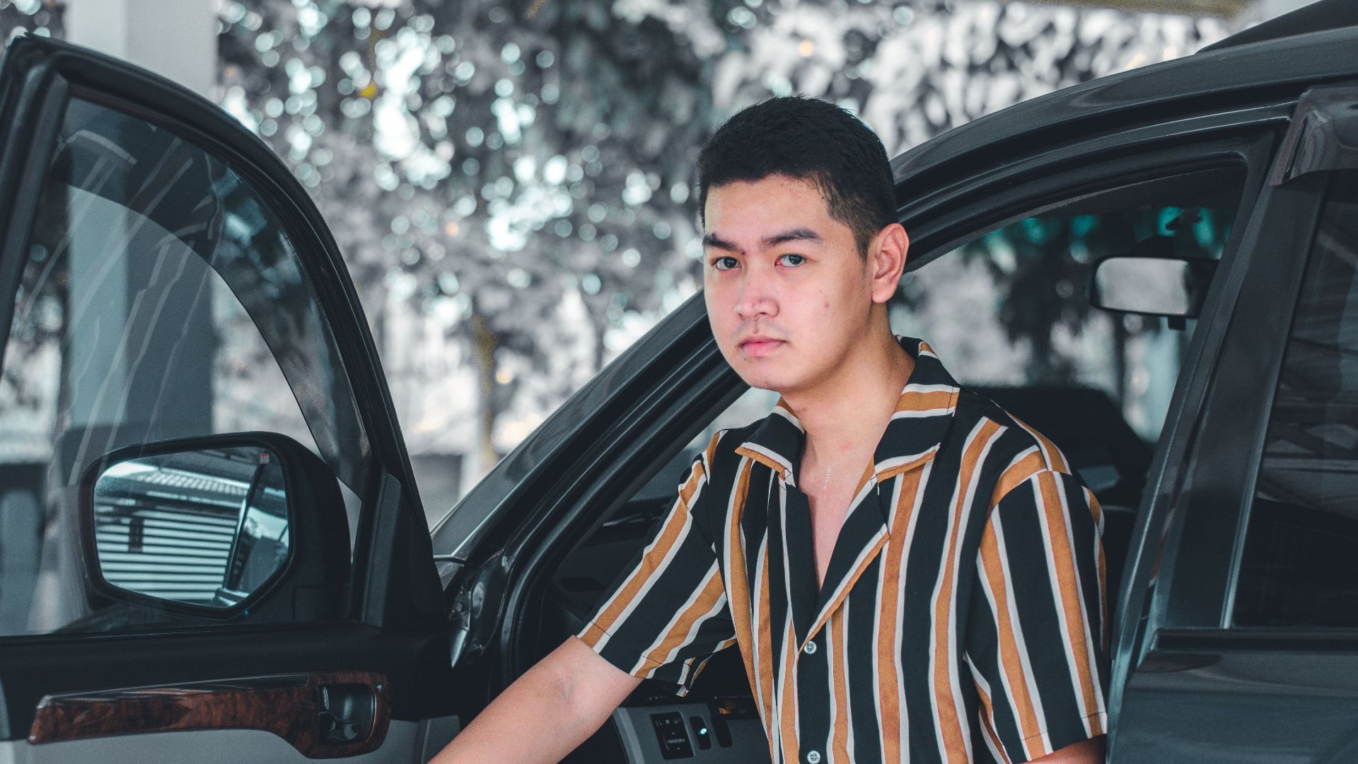 Portrait of a young man with a striped shirt standing beside an open car door.