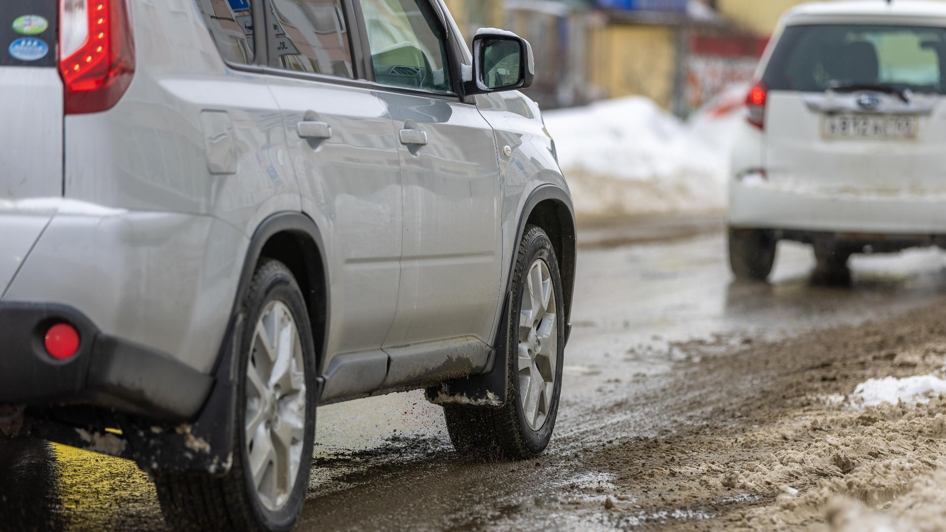 Two cars driving cautiously on a slushy, snowy road during winter.