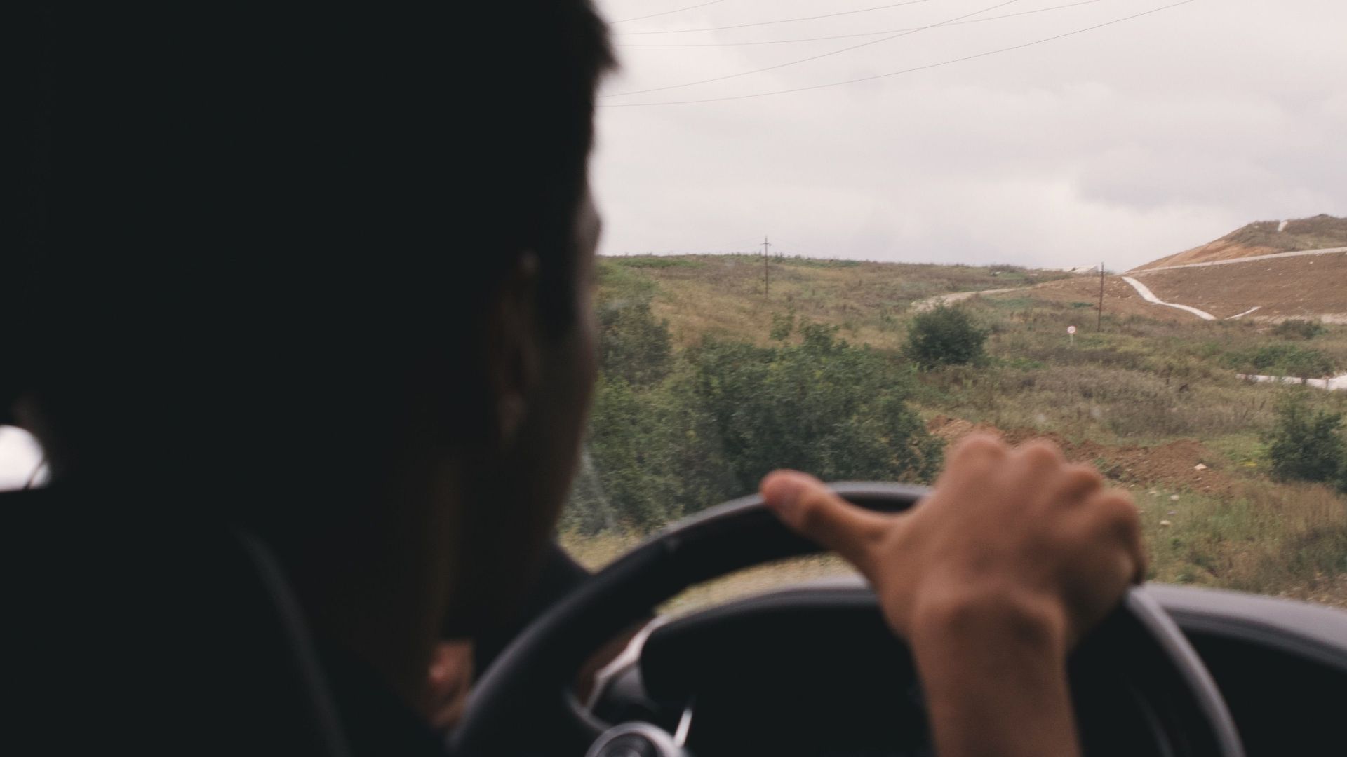Person driving through countryside under an overcast sky, capturing an adventurous mood.