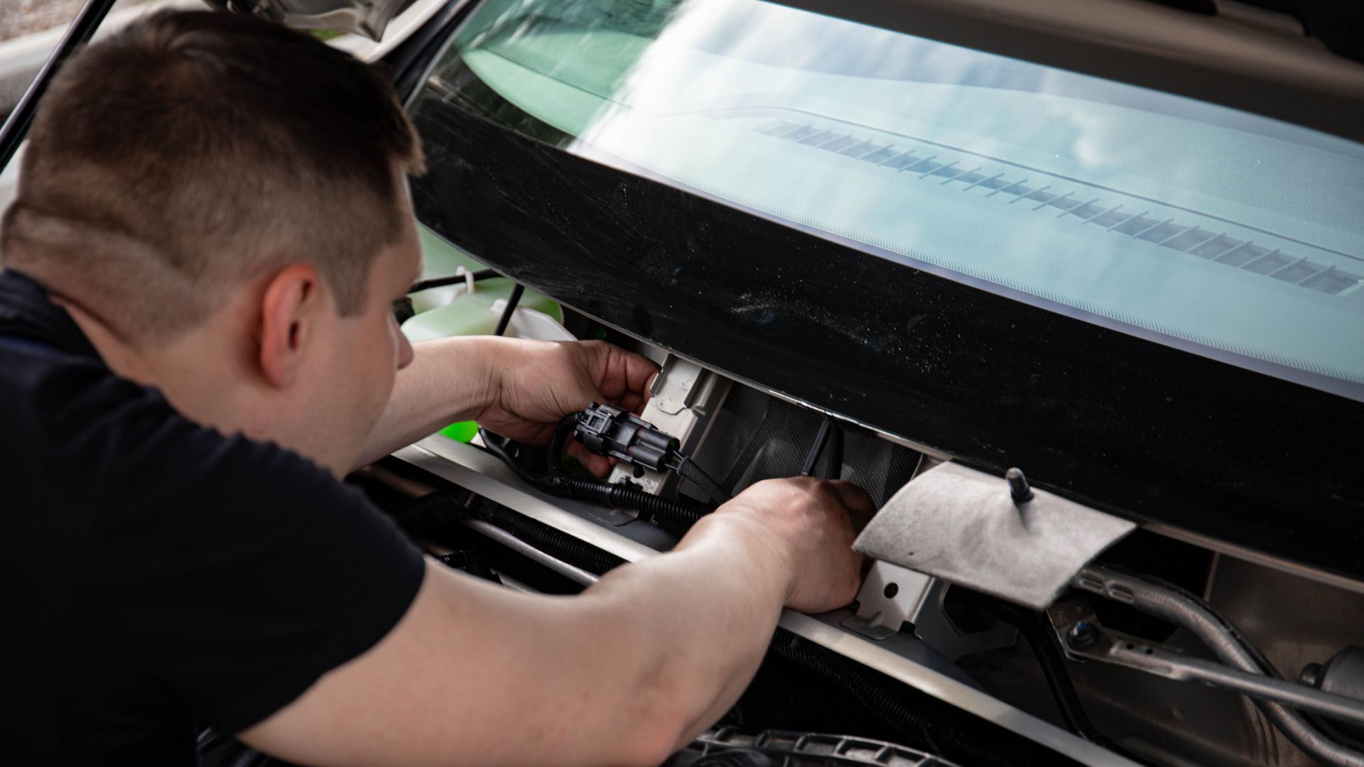 A mechanic working on car engine repairs inside a workshop setting.