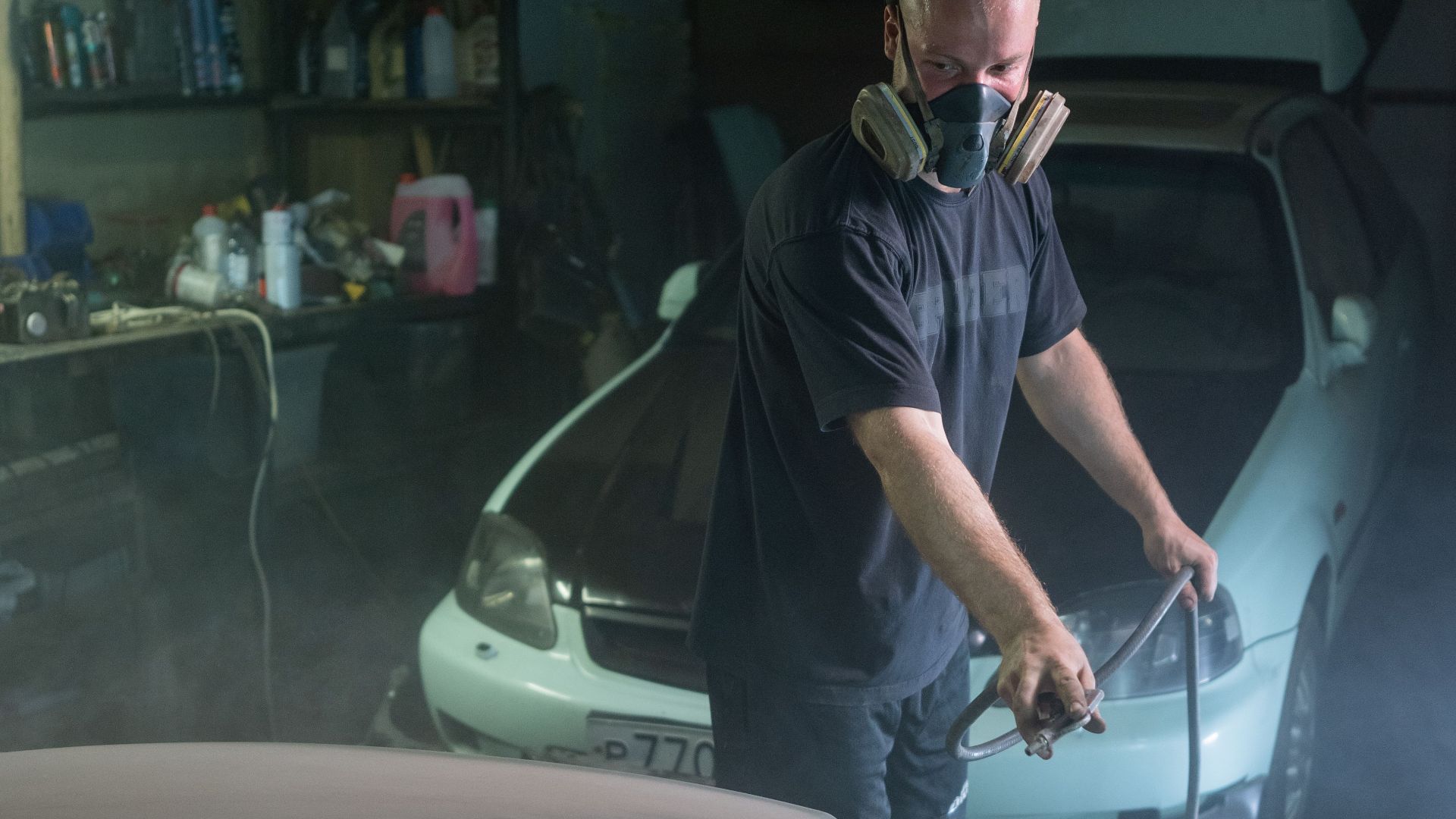 Mechanic wearing a mask spray painting a car in a garage workshop.