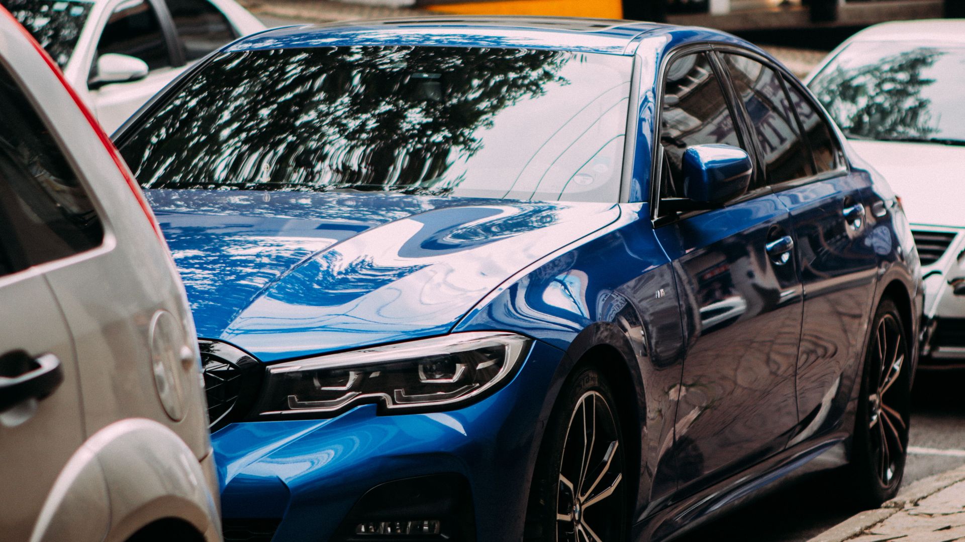 A vibrant blue luxury sedan parked on an urban street among cars.