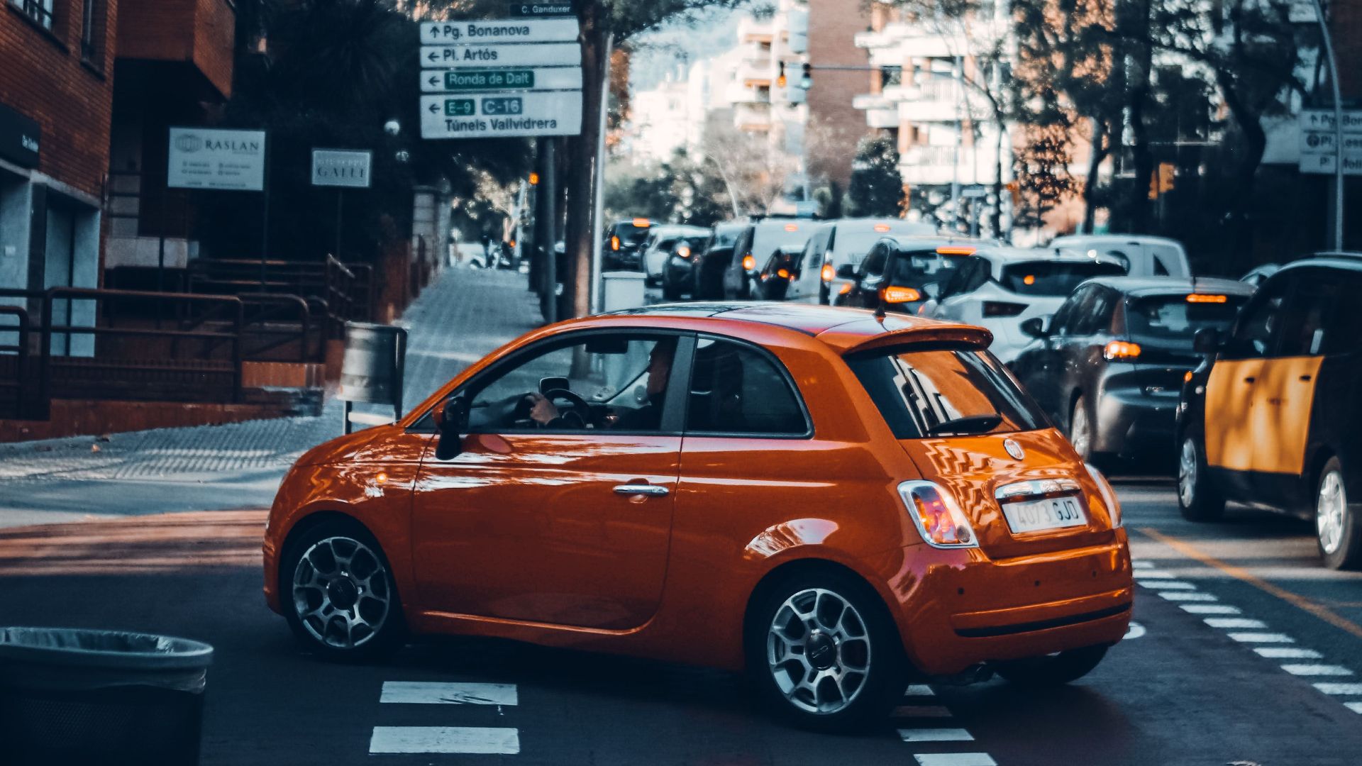 Dynamic scene in a bustling city intersection with an orange car turning amidst traffic.