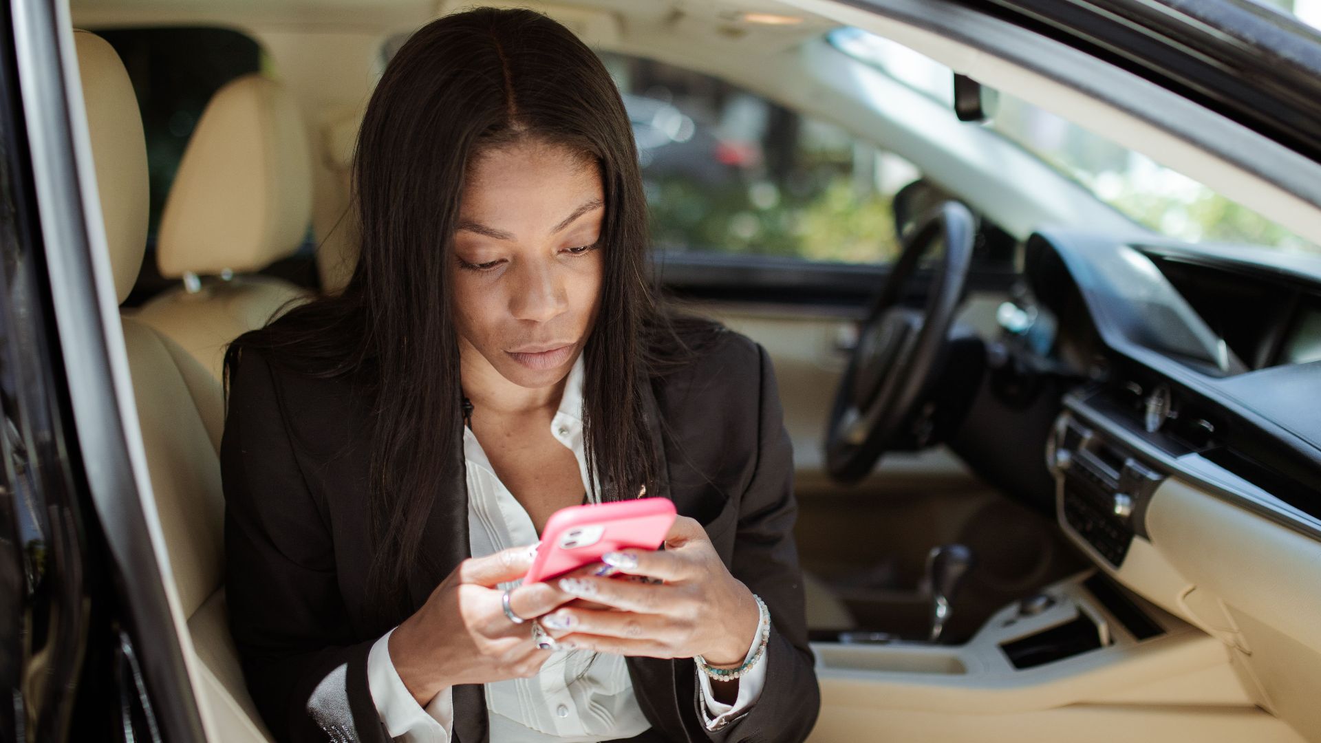 A businesswoman uses her smartphone while seated in a car, focusing intently on the screen.