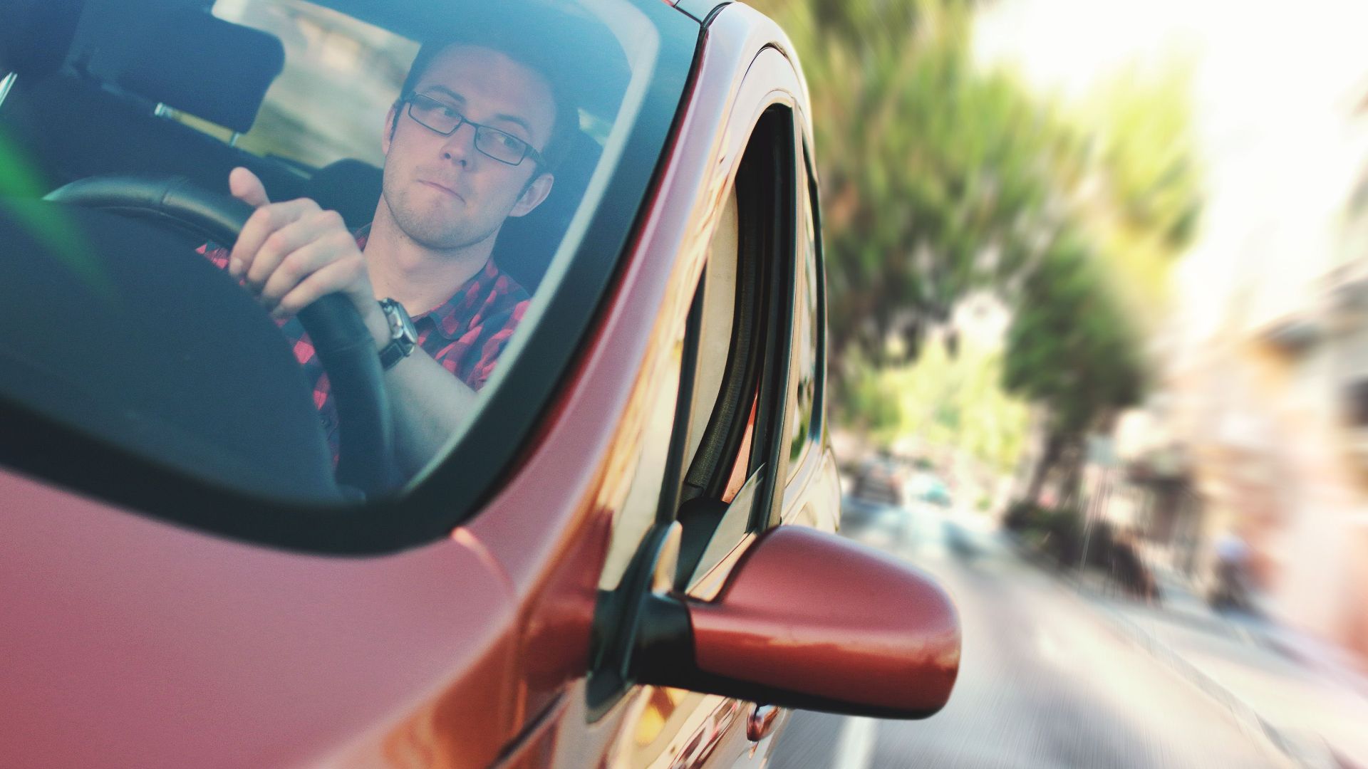 A man driving fast through a city street in a red car, showcasing motion and focus.