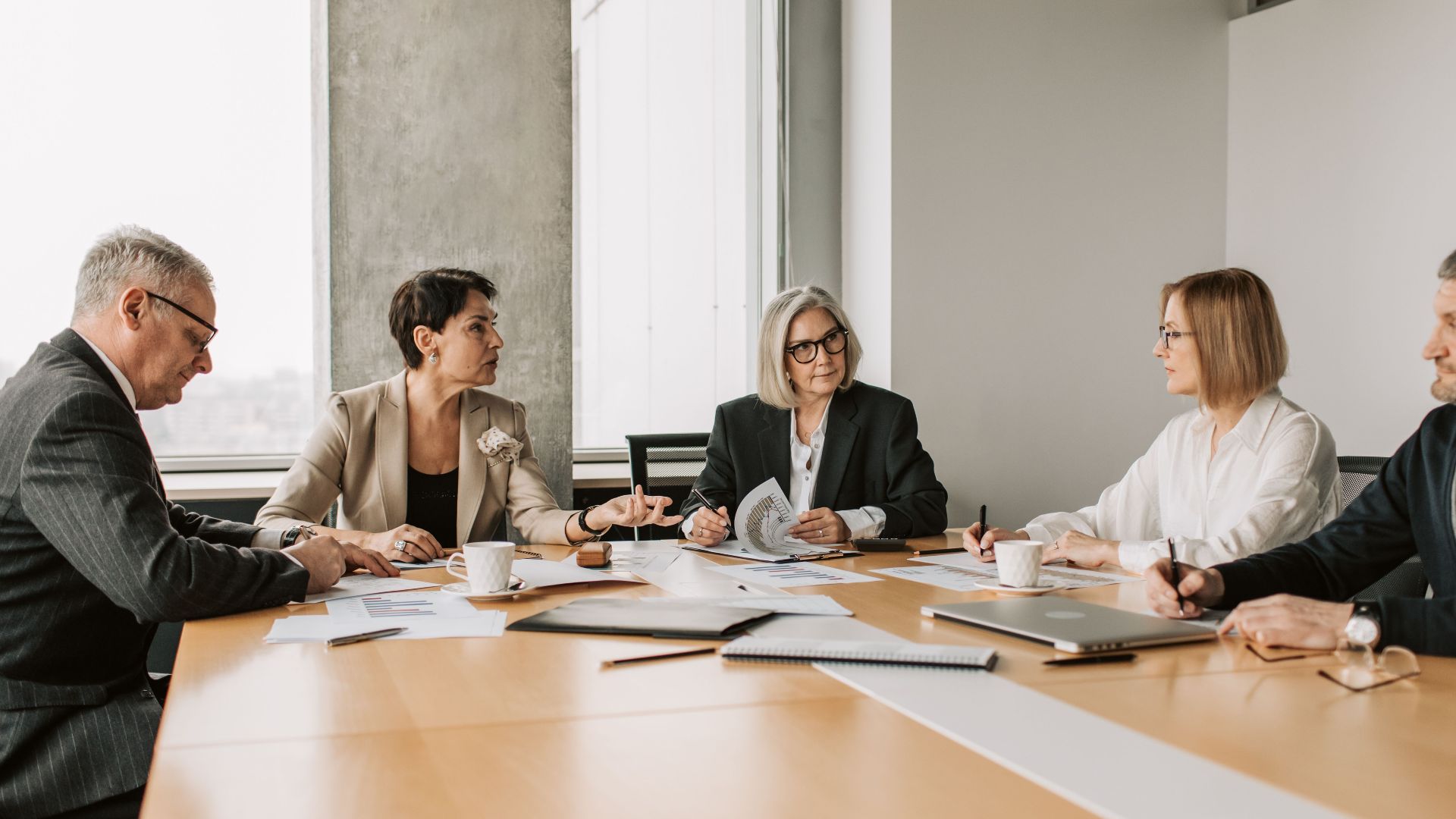 Five business professionals engaged in a meeting in a modern office setting, discussing documents and ideas.