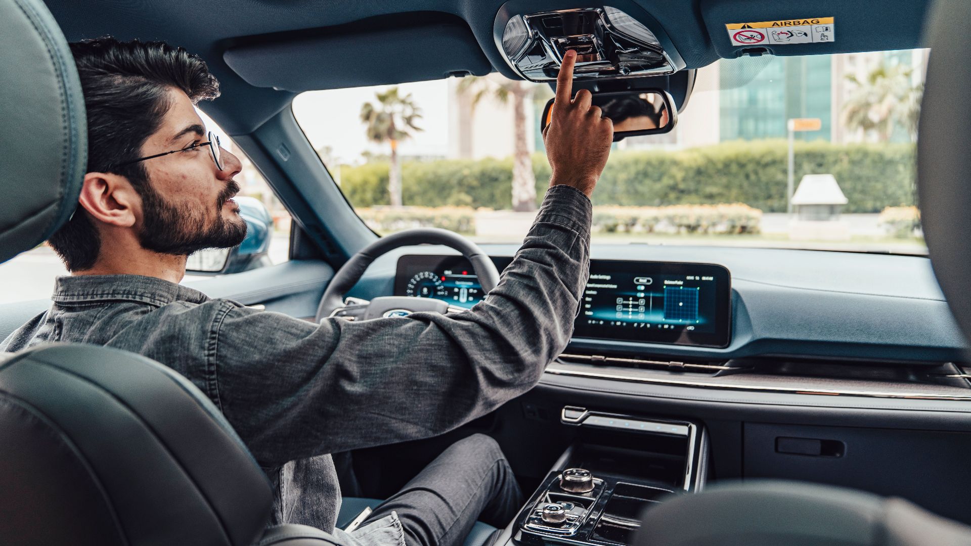 A man adjusts the interior features of a modern car while driving in Erbil, Iraq.