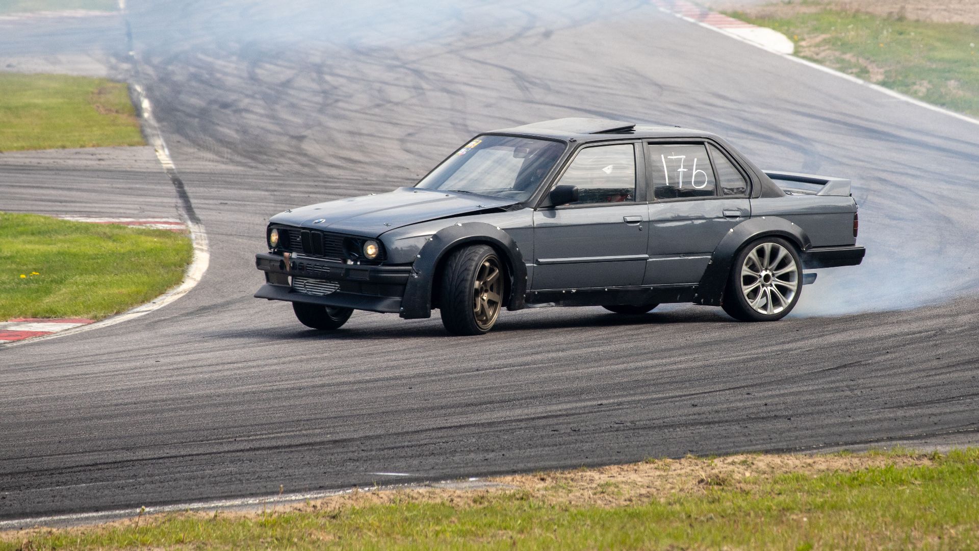 An action-packed shot of a car drifting on a racetrack, trails of smoke follow the wheels as it rounds the bend.