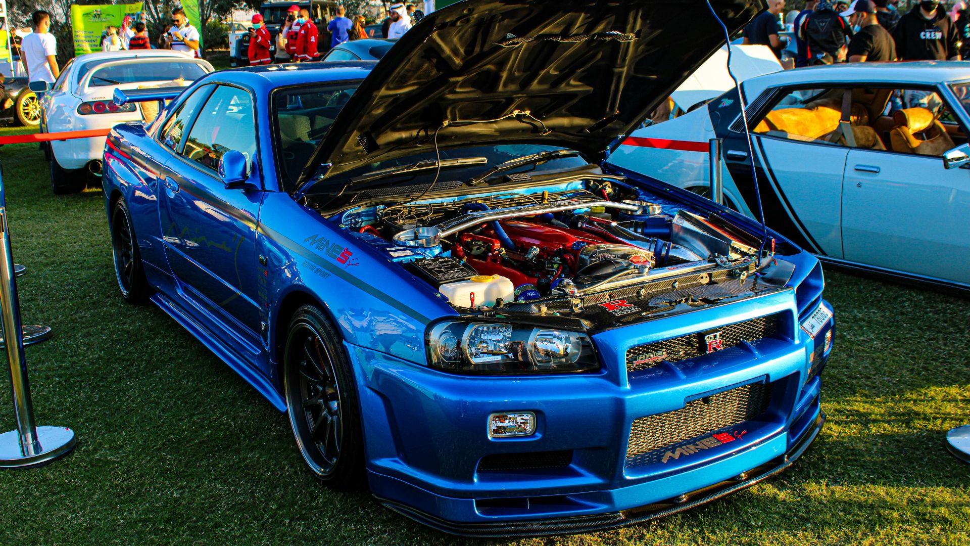 A blue Nissan Skyline GT-R with an open hood at an outdoor car show
