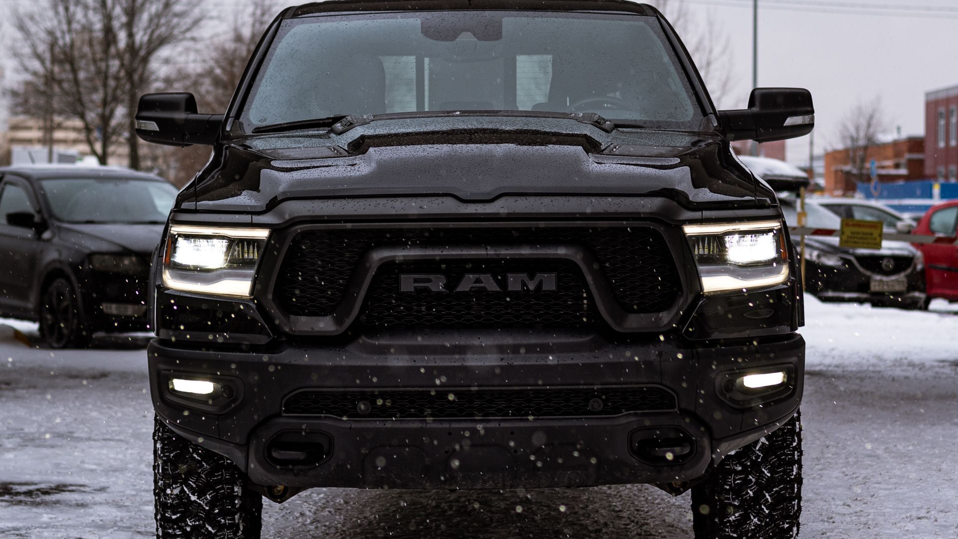Front view of a black Dodge Ram 1500 Rebel parked under a bridge in a snowy urban area.