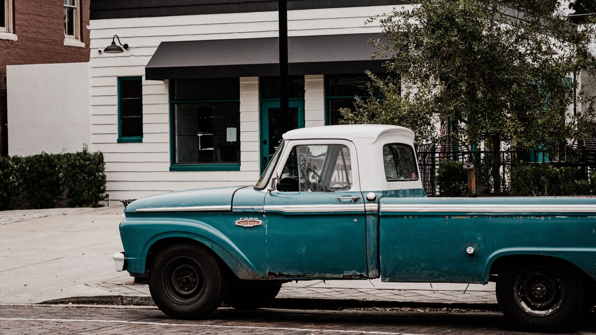 Classic blue pickup truck parked on a cobblestone street in front of vintage buildings.