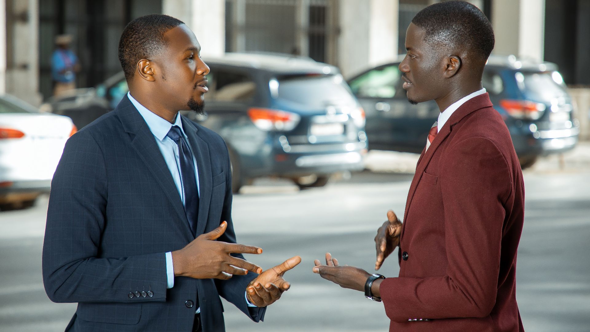 Two African businessmen in formal suits have a discussion on a city street in Dakar, Senegal.