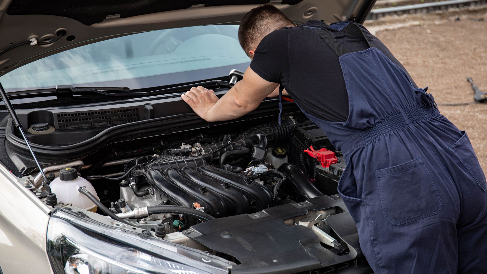 Mechanic checking car engine outdoors, focusing on vehicle maintenance and repair.