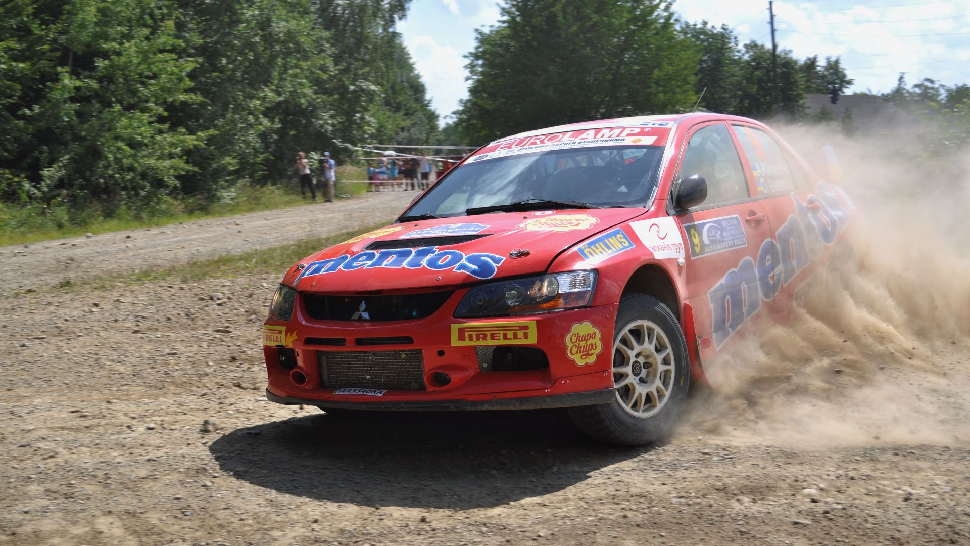 Red Mitsubishi Lancer Evo speeding through a dirt track during a thrilling rally race with dust clouding behind.