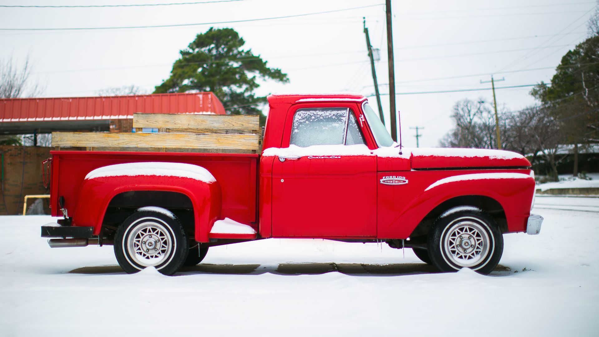Bright vintage pick up truck parked on snowy terrain against construction and lamp post on winter day