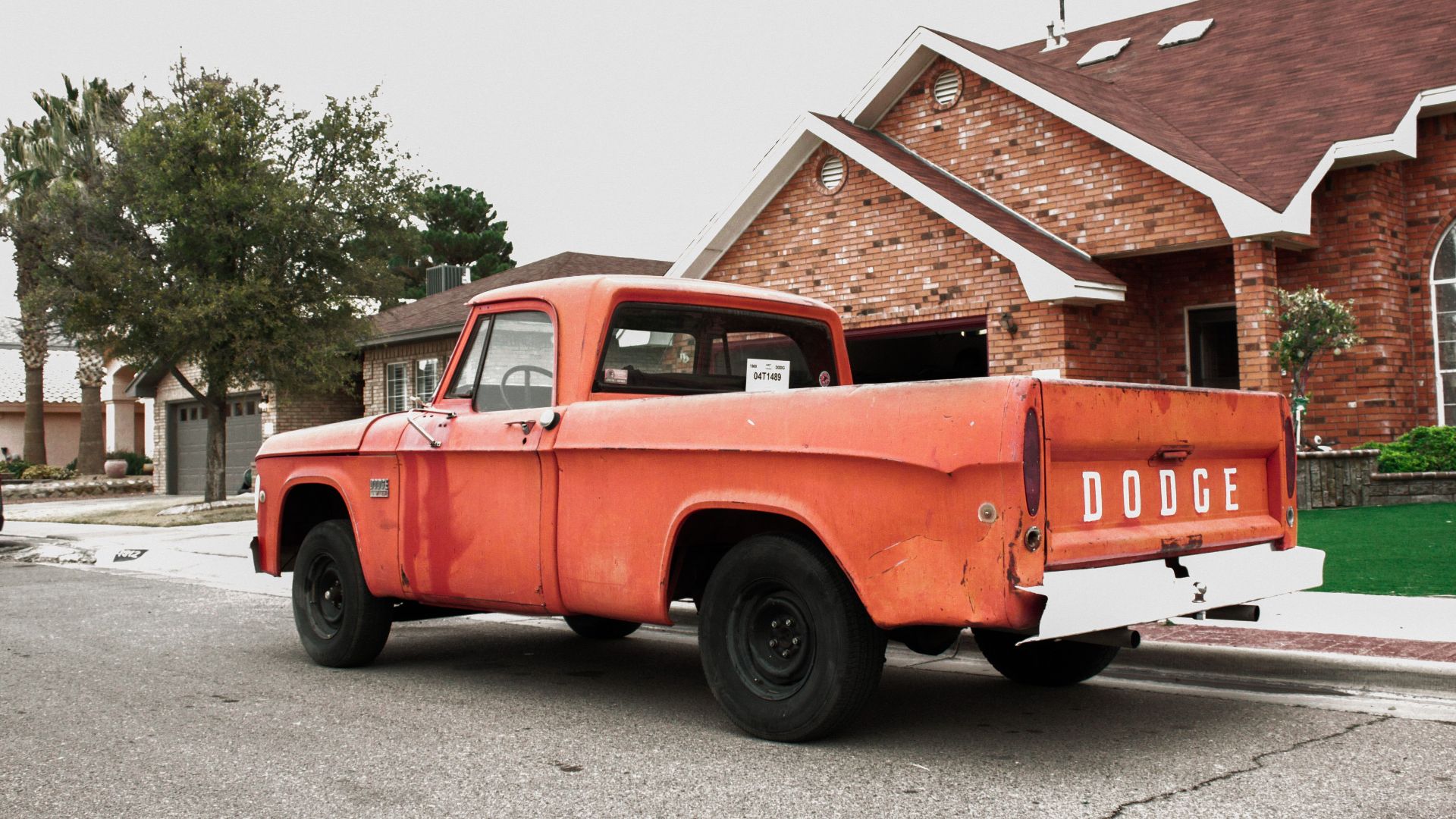 Old red Dodge truck parked in a quiet suburban neighborhood street.