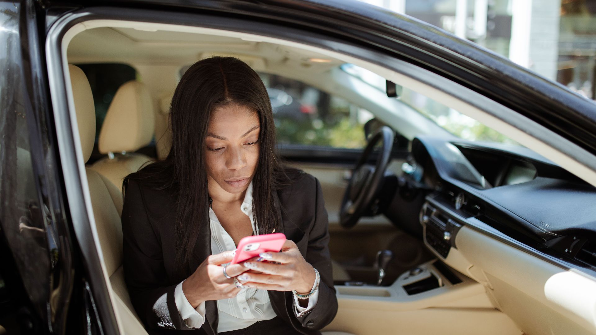 A businesswoman uses her smartphone while seated in a car, focusing intently on the screen.