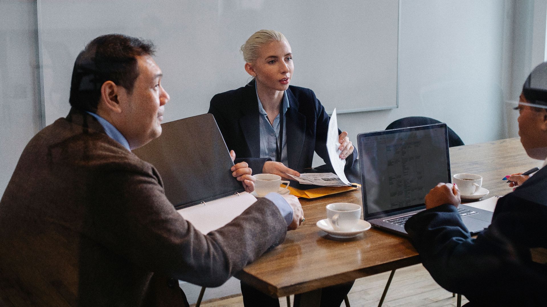Multiracial colleagues in formal clothes sitting at table with laptop and documents while discussing details of business plan