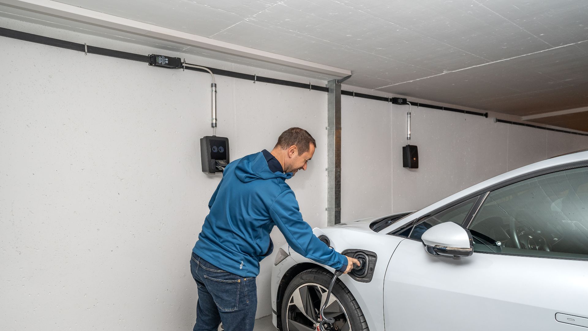 A man connects an electric car to a charging station in a modern indoor garage setting.