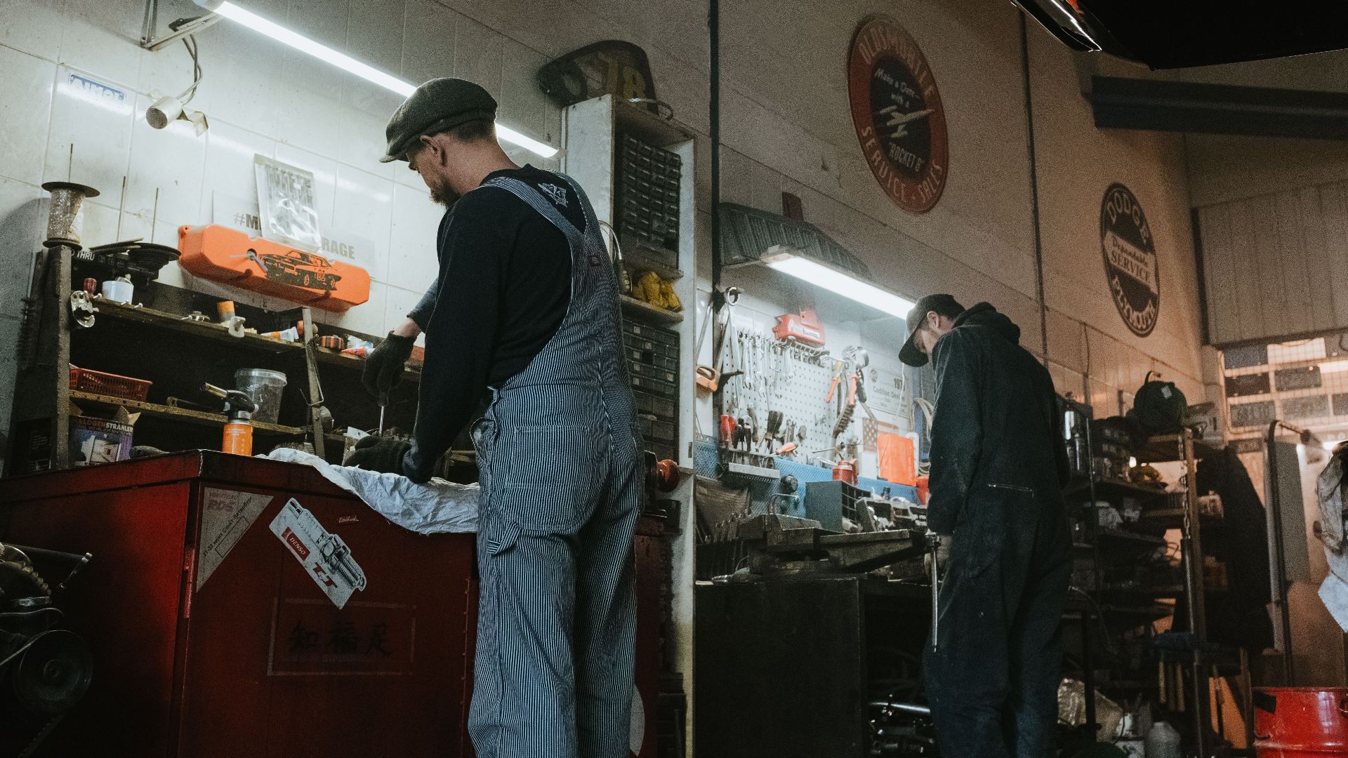 Two mechanics in a garage working on vehicle repair and maintenance.