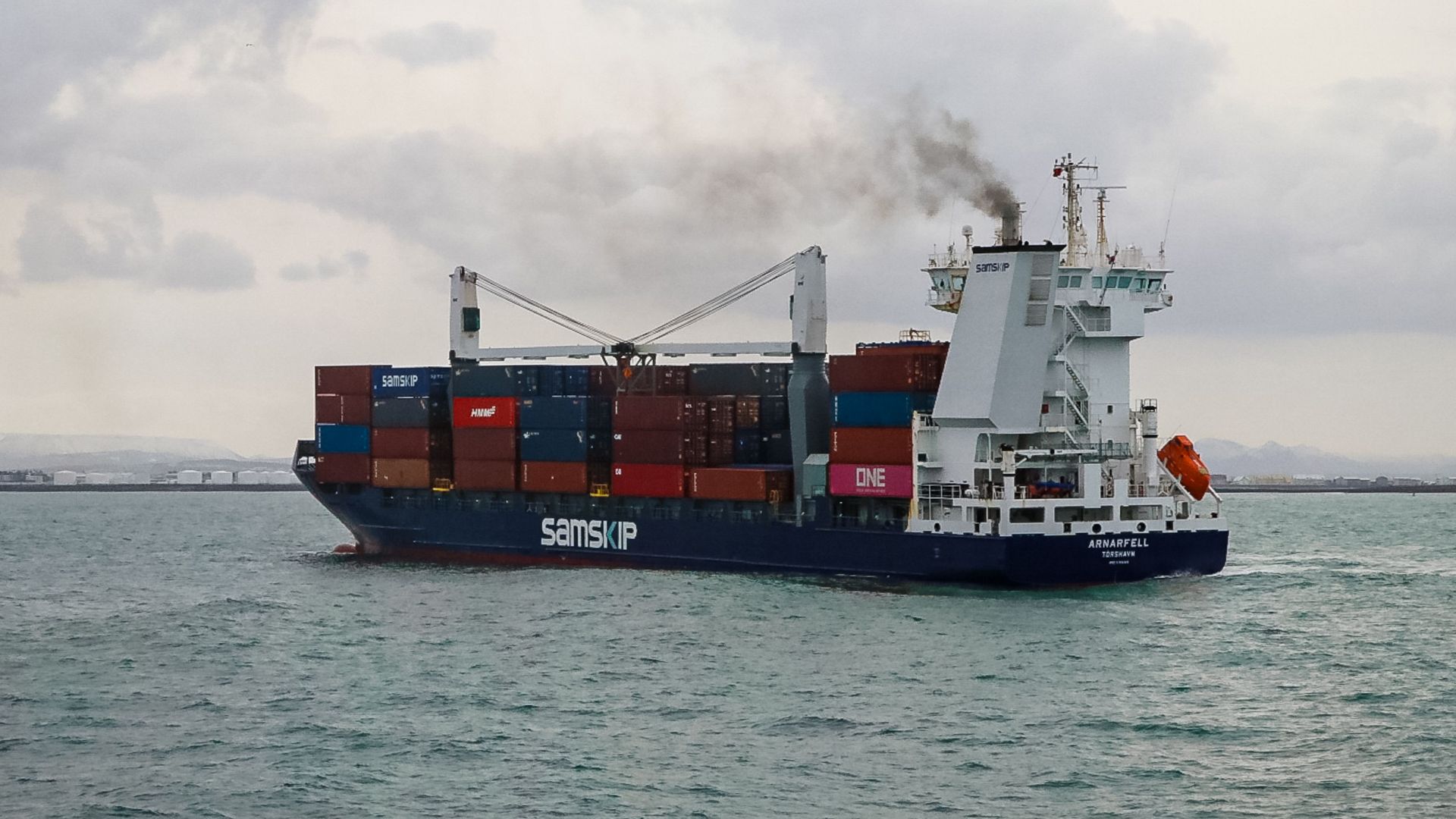 Commercial cargo ship transporting goods across Icelandic waters under a cloudy sky.