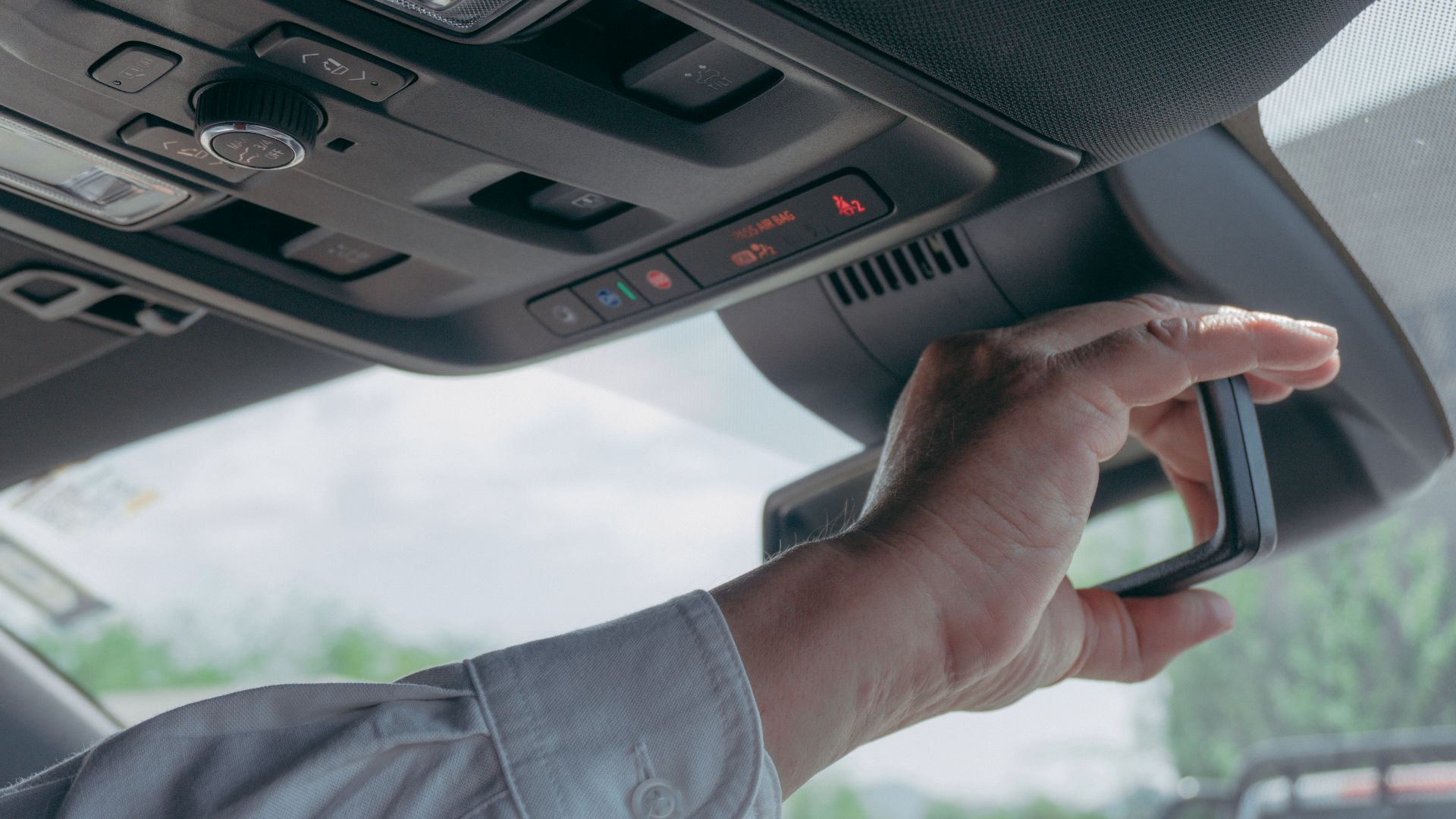 Close-up of a driver adjusting the rearview mirror inside a car, showcasing modern vehicle technology.