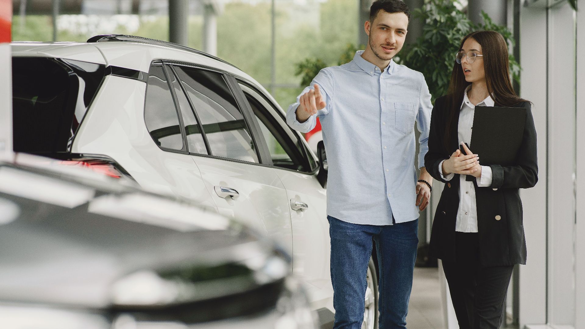 Customer and salesperson discussing a vehicle inside a modern car dealership showroom.