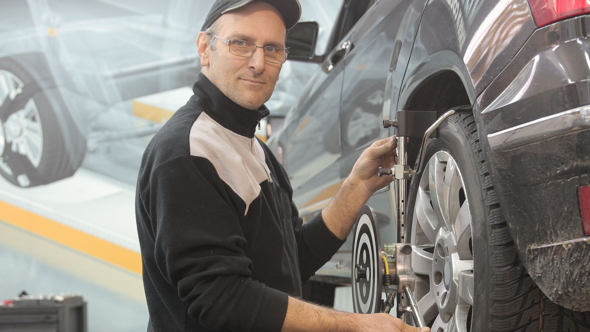 Mechanic performing wheel alignment on a car in a professional garage setting.