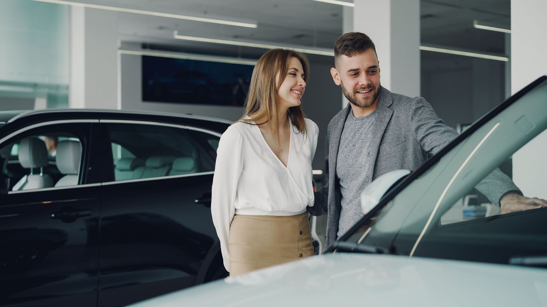 Smiling couple exploring cars at dealership, enjoying shopping experience.