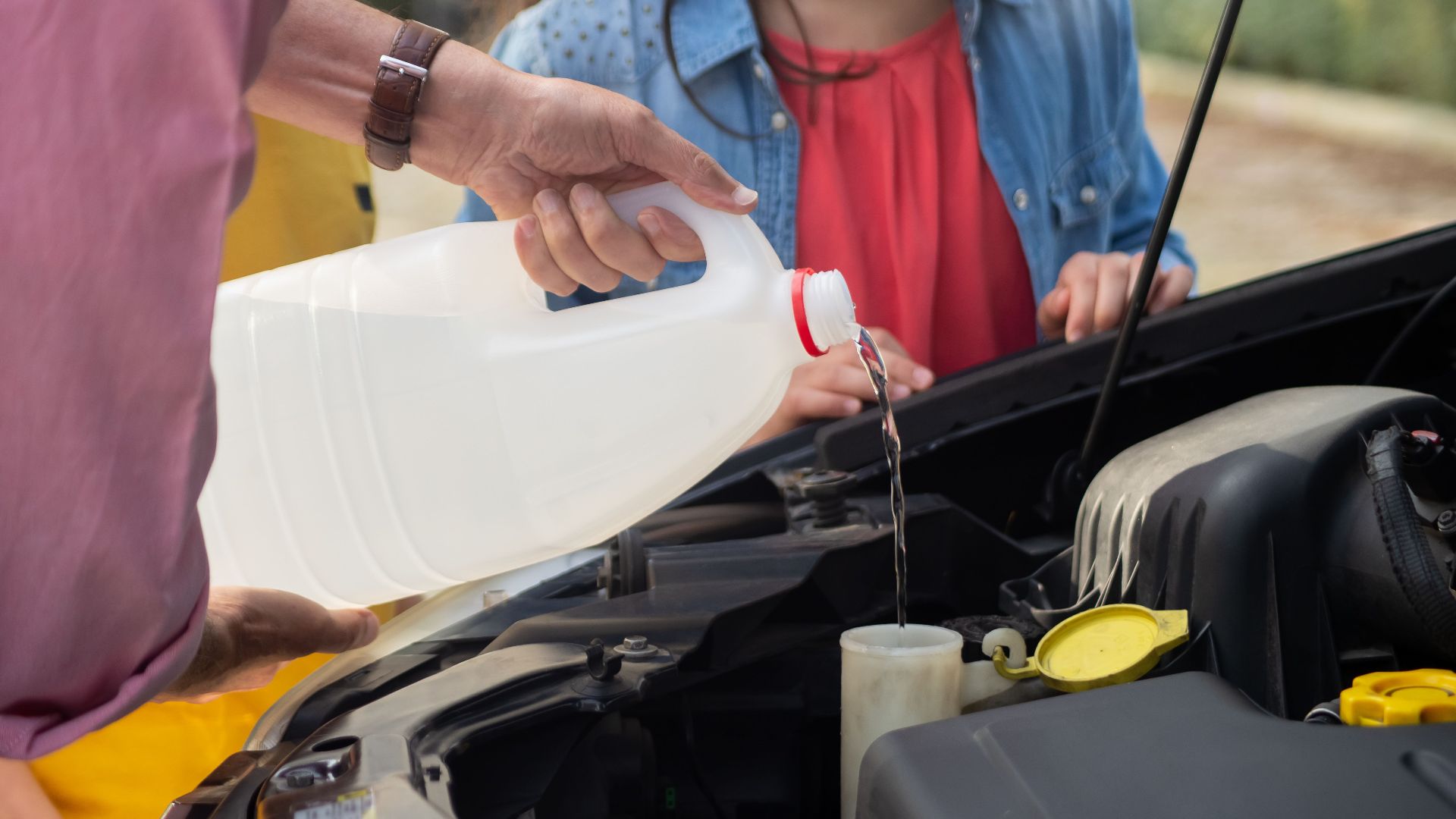 Close-up of a person pouring windshield washer fluid into a car, emphasizing vehicle maintenance.