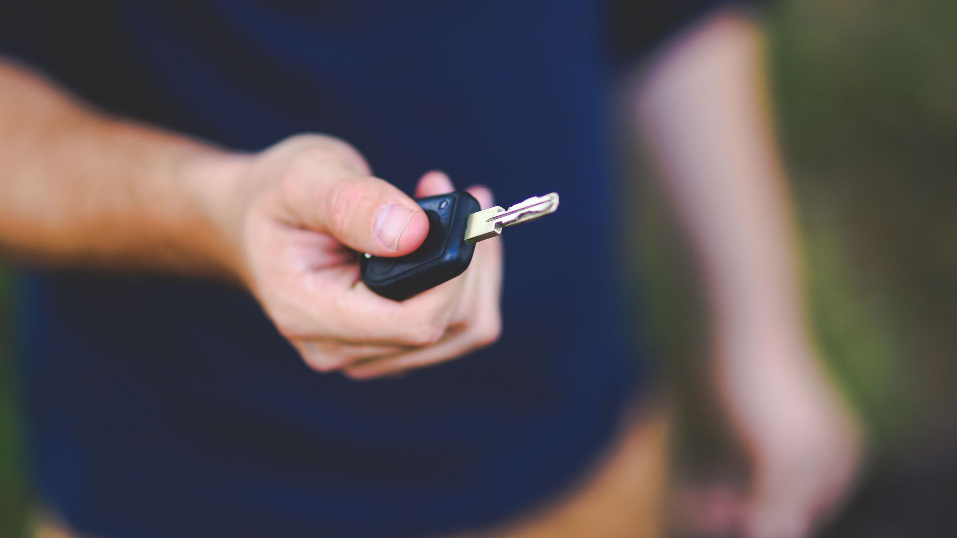 A hand holding a car key outdoors, emphasizing security and control.