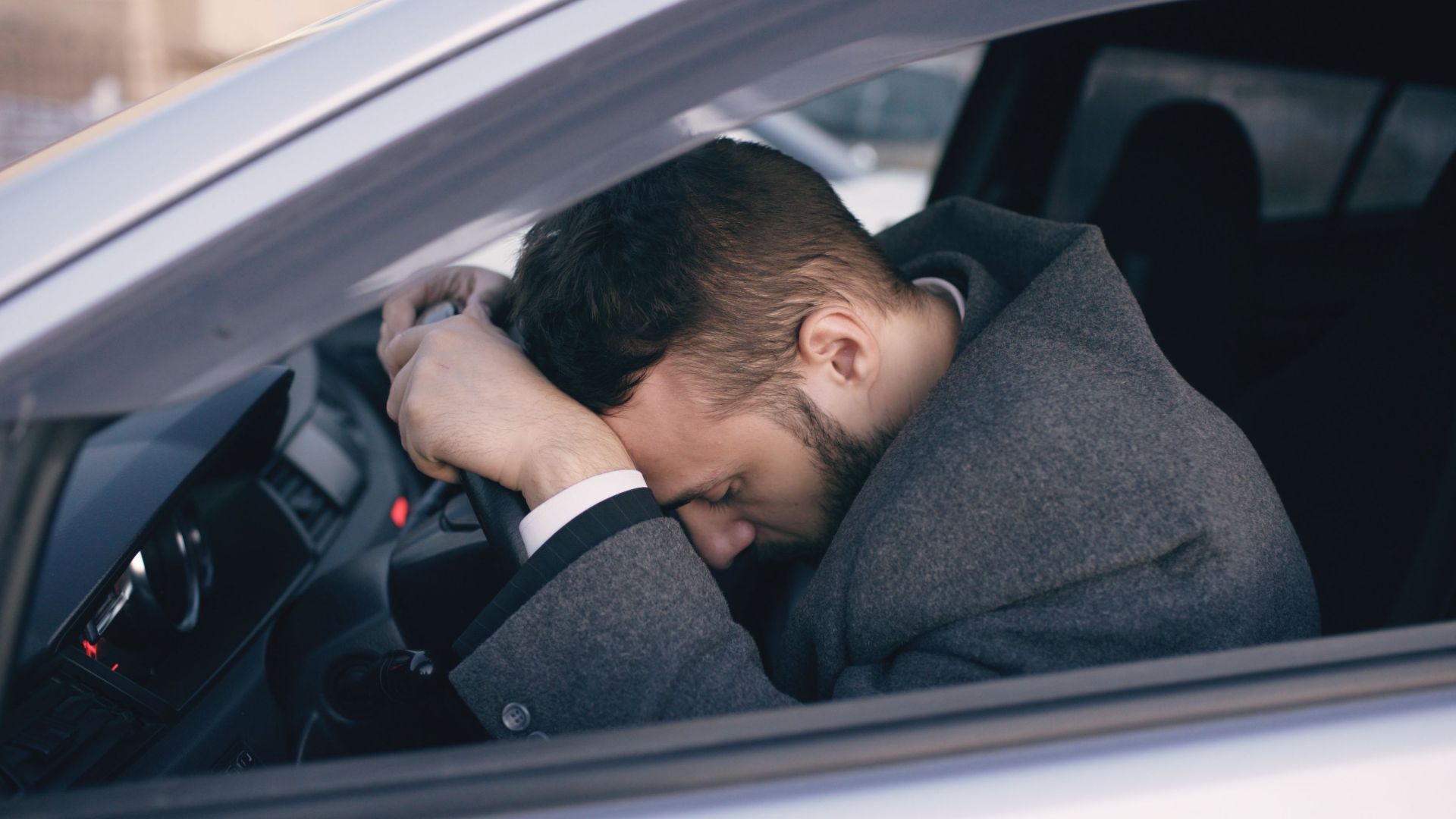 Man in car showing stress with head on steering wheel, highlighting emotional fatigue.