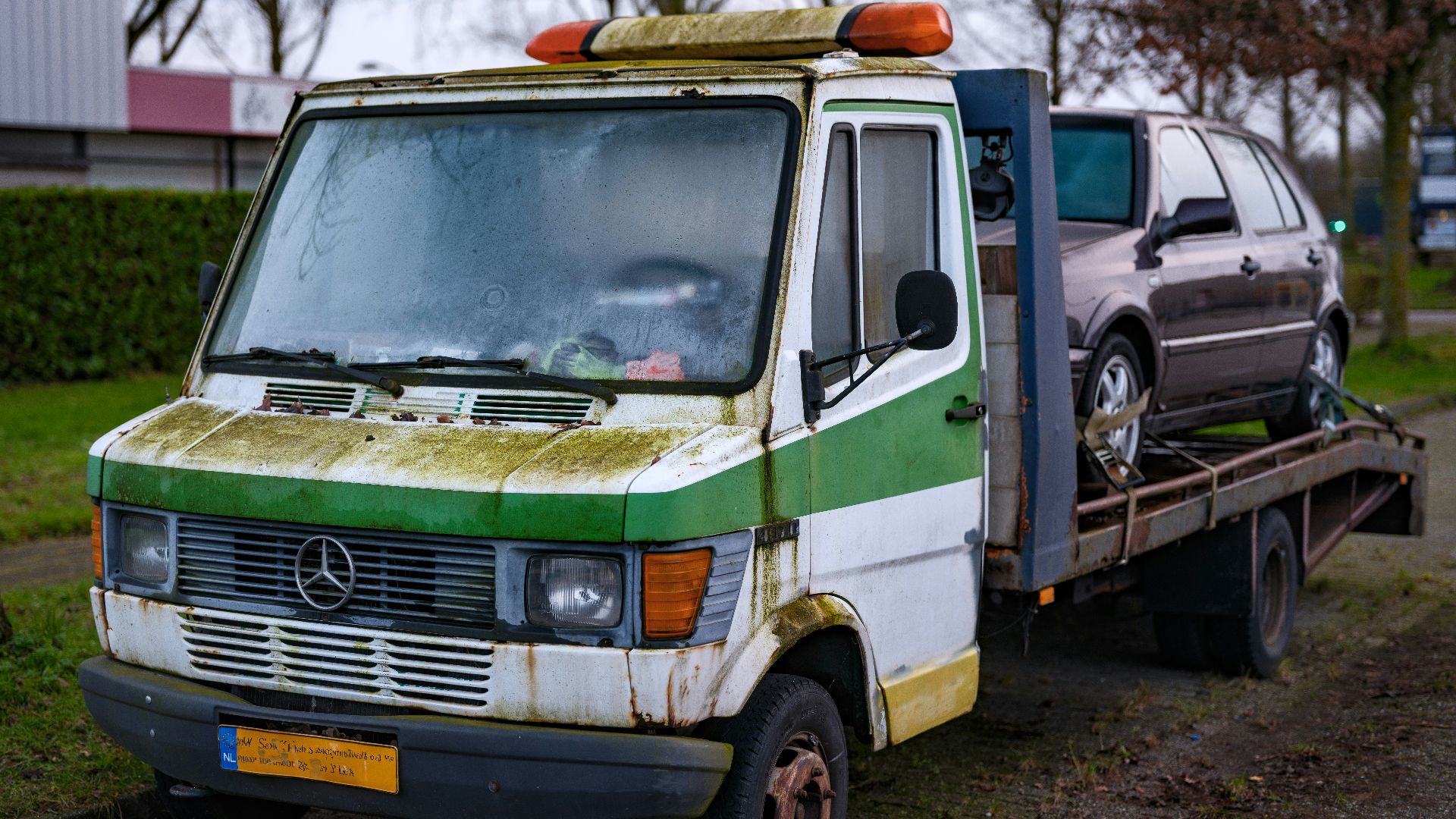 An old green and white van is being towed by a tow truck