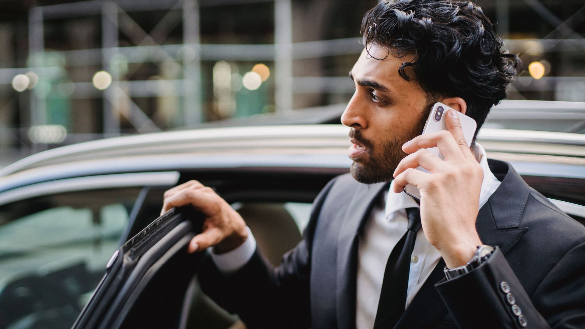 A businessman in a suit talking on his smartphone while exiting a vehicle.
