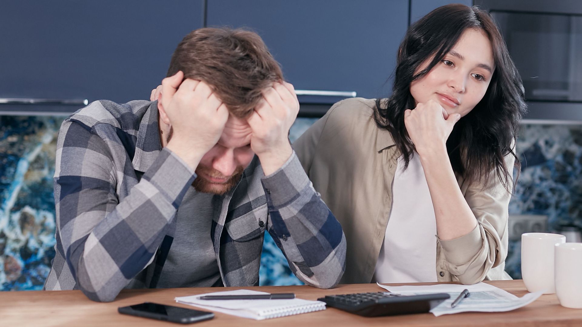 A couple looking worried while reviewing financial documents at a kitchen table.