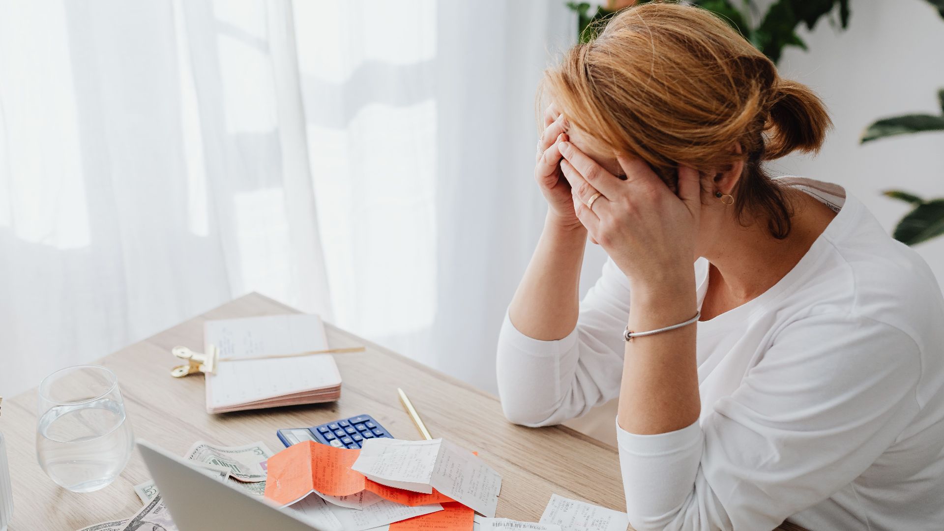 Woman stressed over financial receipts at a desk, dealing with expenses and calculations.