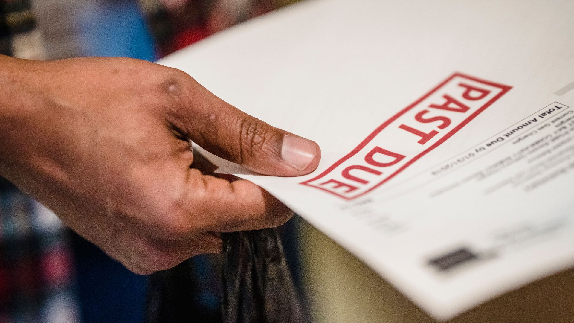 A close-up of a hand holding a document with a 'Past Due' stamp, highlighting financial urgency.