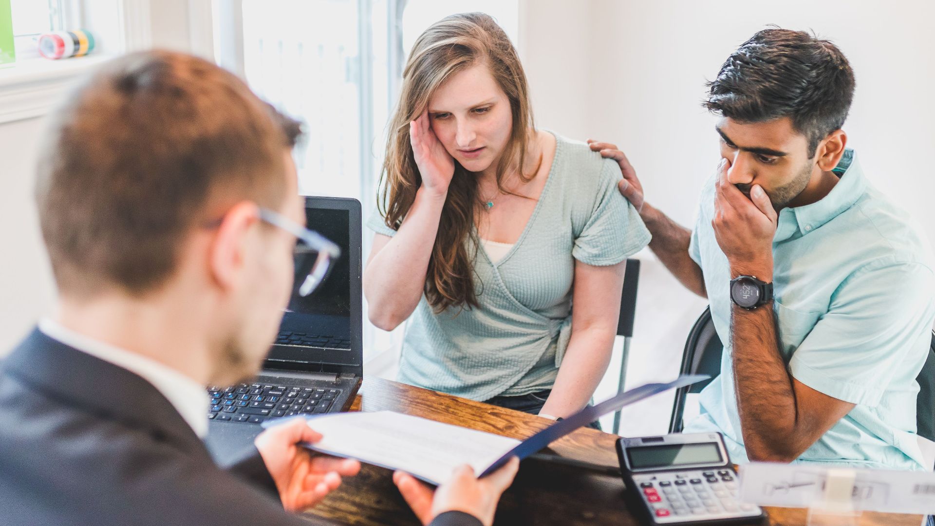 A worried couple consults with a real estate agent about home buying processes.