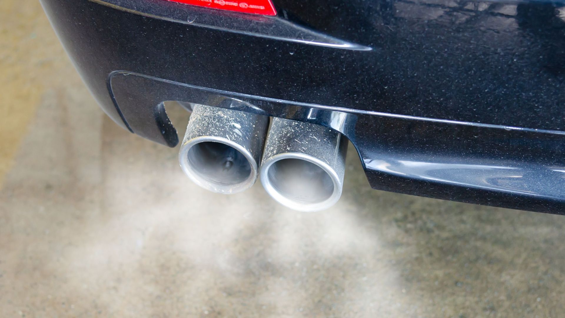 Close-up of a car's exhaust pipes emitting visible smoke, highlighting air pollution.